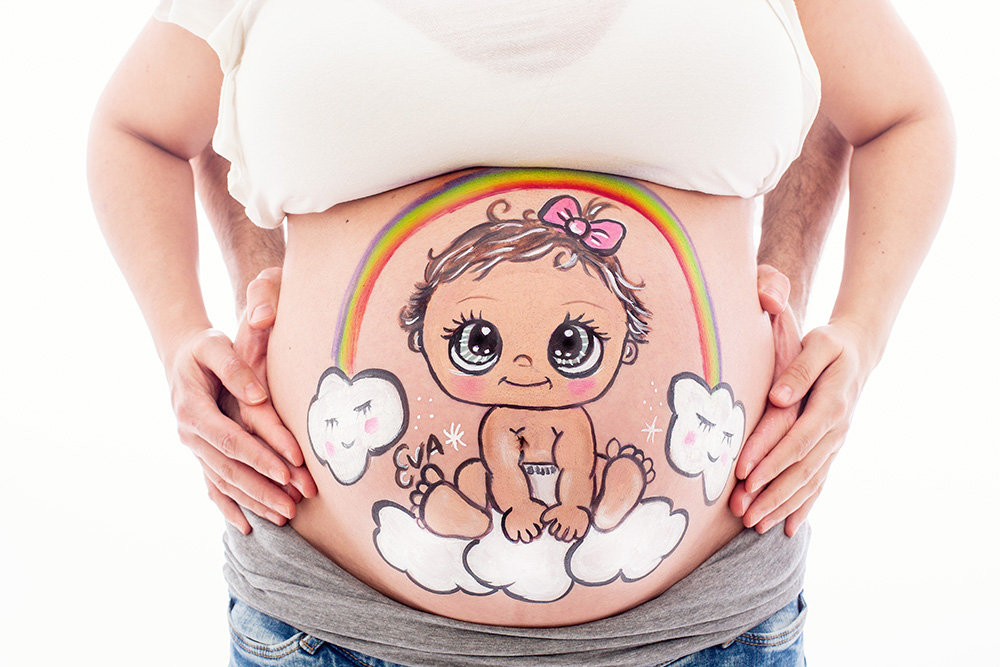 foto de barriguita pintada de una mujer embarazada con un dibujo de un bebe arcoiris y unas nubes