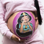 Foto de barriguita pintada de una embarazada en la que hemos pintado un dibujo de la princesa Jasmine con tonos Morados,rosas y azules